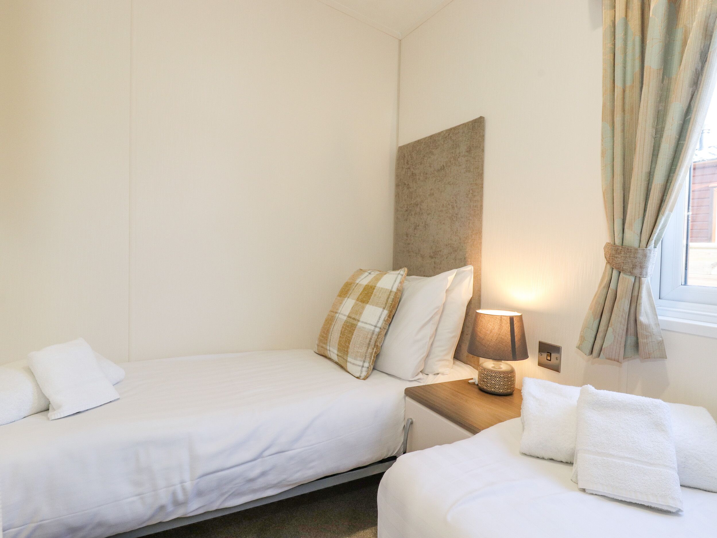 Een hotelkamer met twee bedden, een nachtkastje met een lamp en een raam met gordijnen.