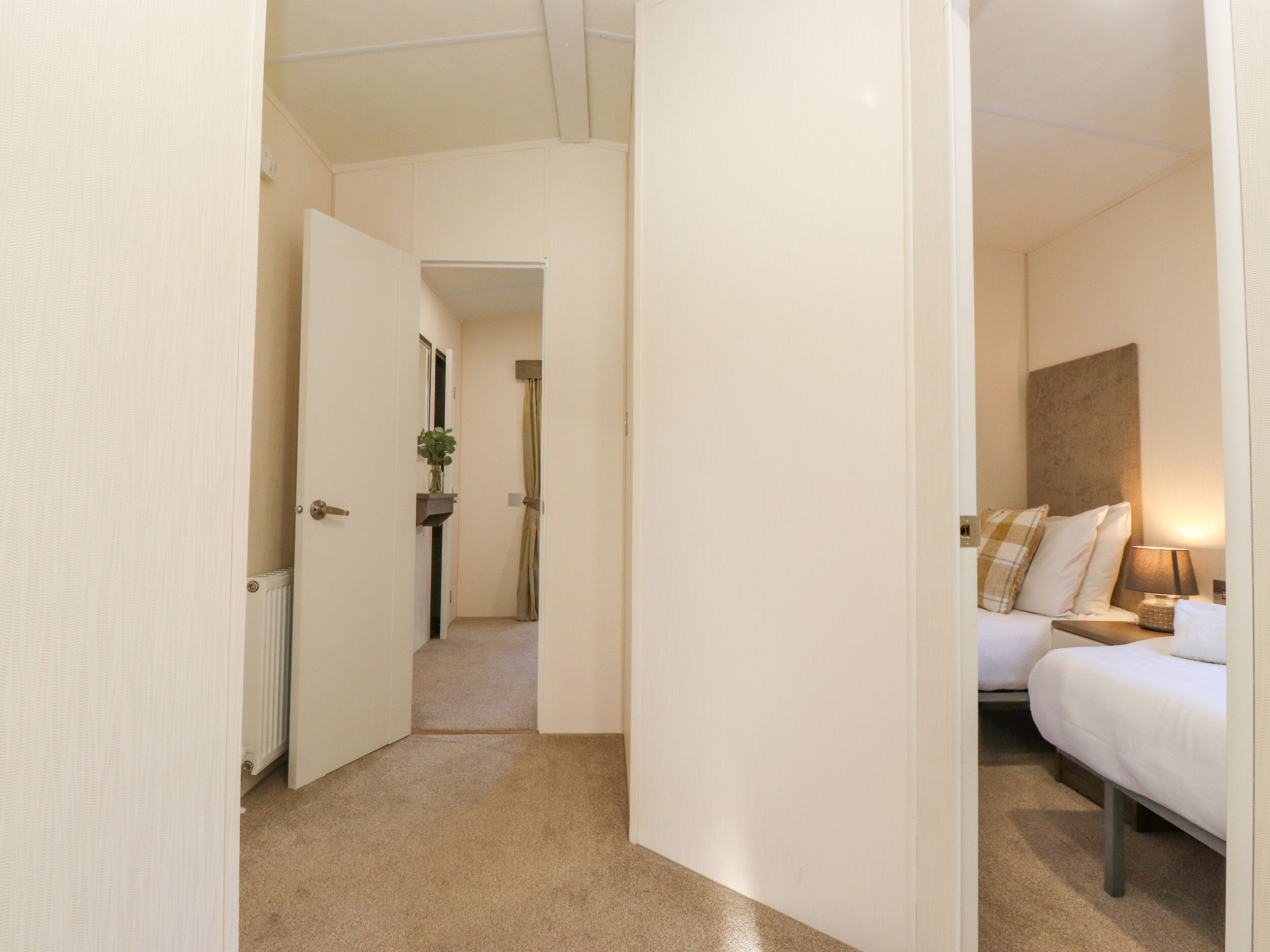 A hotel room with a bed, bedside table, lamp, and a view of the hallway.