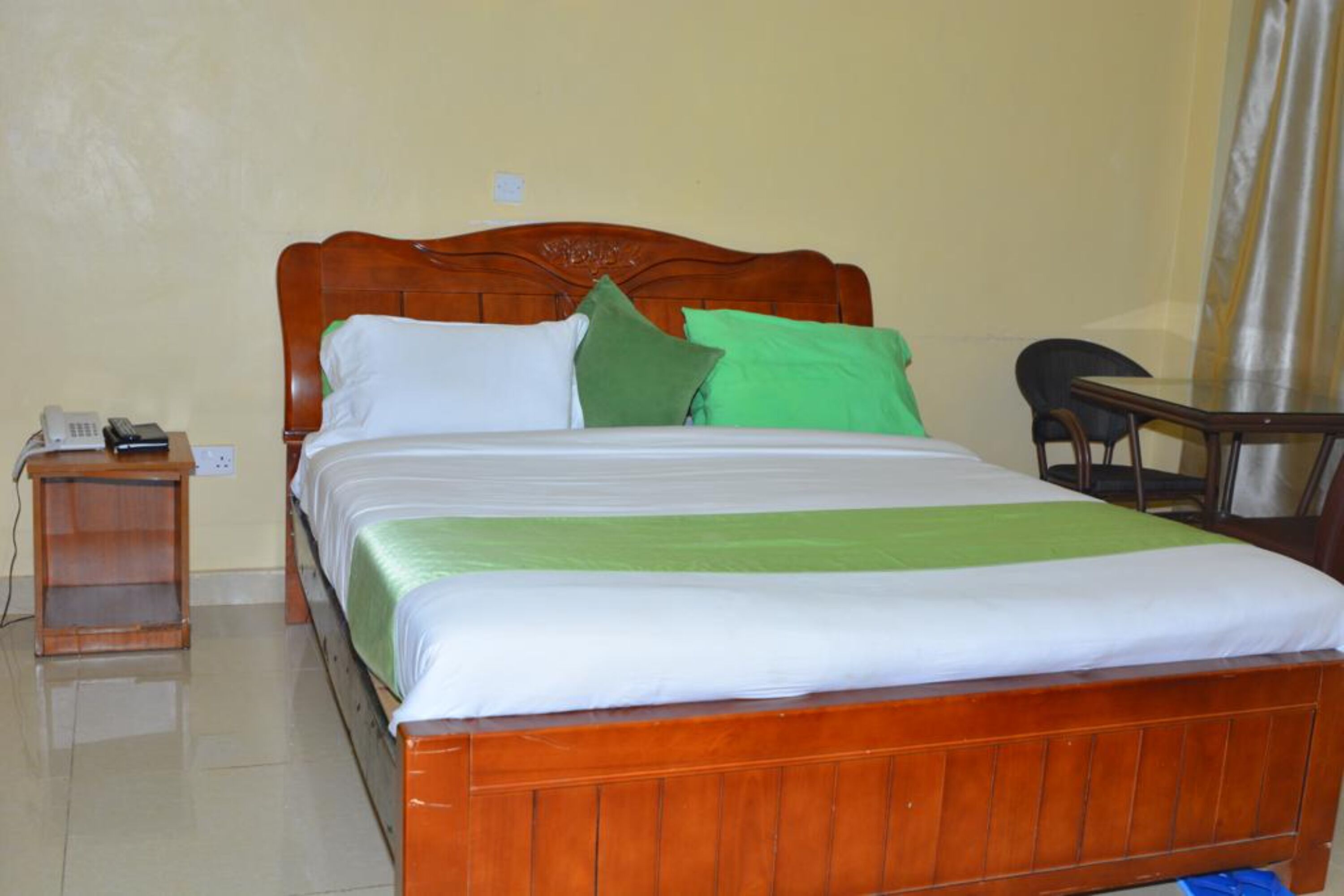 A neatly made bed with a wooden headboard, a bedside table with a phone, and a chair to the right.