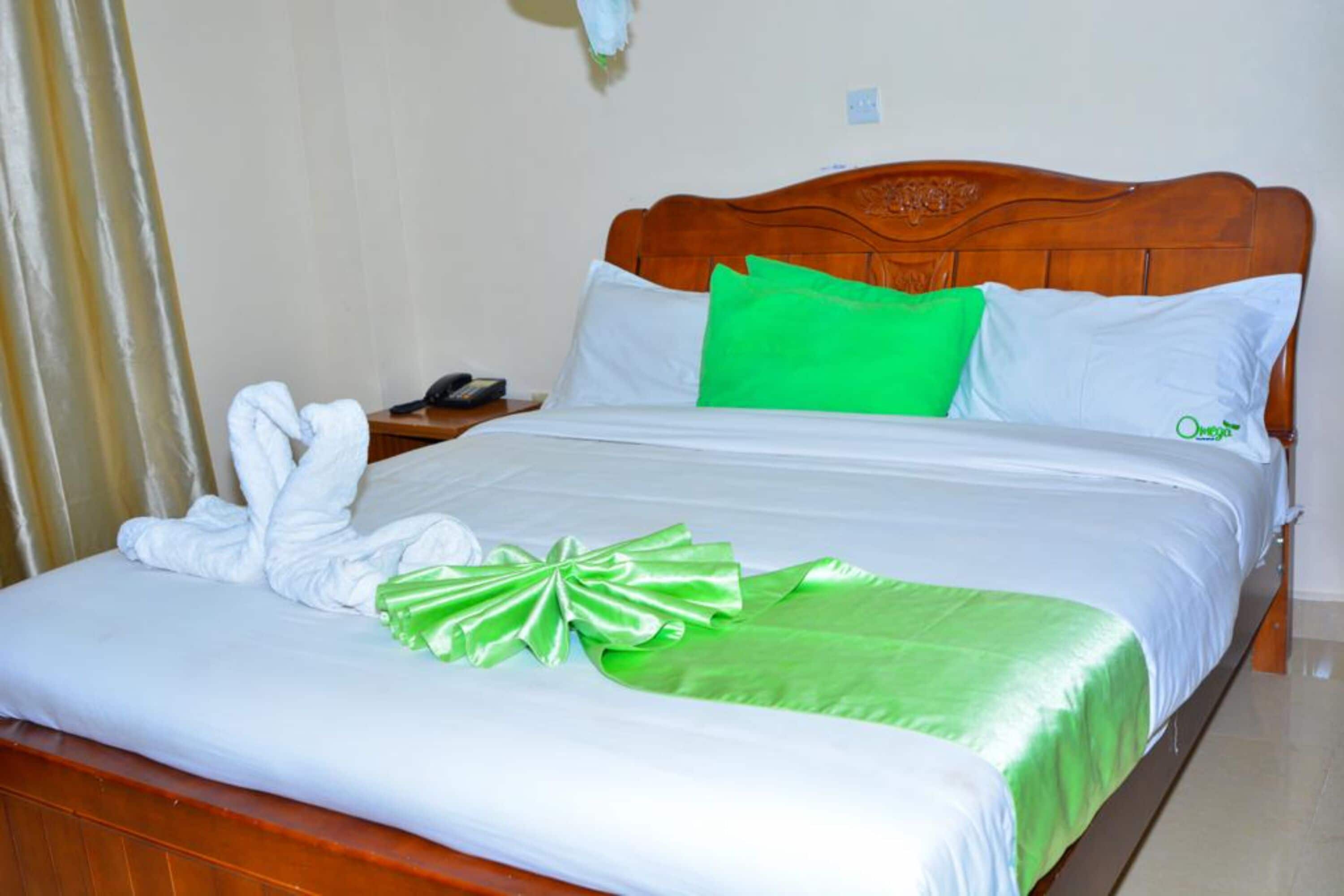 A neatly made bed with white linens, a green pillow, and a green decorative bow.