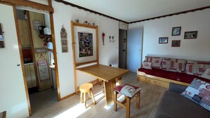 A cozy living room with a wooden table, a small stool, and a sofa with patterned cushions. - Cozy studio at the foot of the slopes in Plagne Village (Plagne Villages)