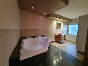 Une salle de bain moderne avec une baignoire sur pieds, un meuble-lavabo avec un miroir et une fenêtre laissant entrer la lumière naturelle.
