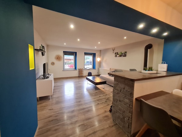 Ein modernes Wohnzimmer mit einer Wand aus Naturstein, einem weißen Sofa, einem Esstisch und einer Küchenzeile mit Herd.