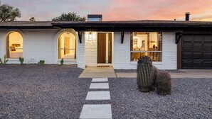 Une maison moderne à l’extérieur blanc, dotée d’un portail en arc de pierre et d’une allée gravillonnée menant à la porte d’entrée.