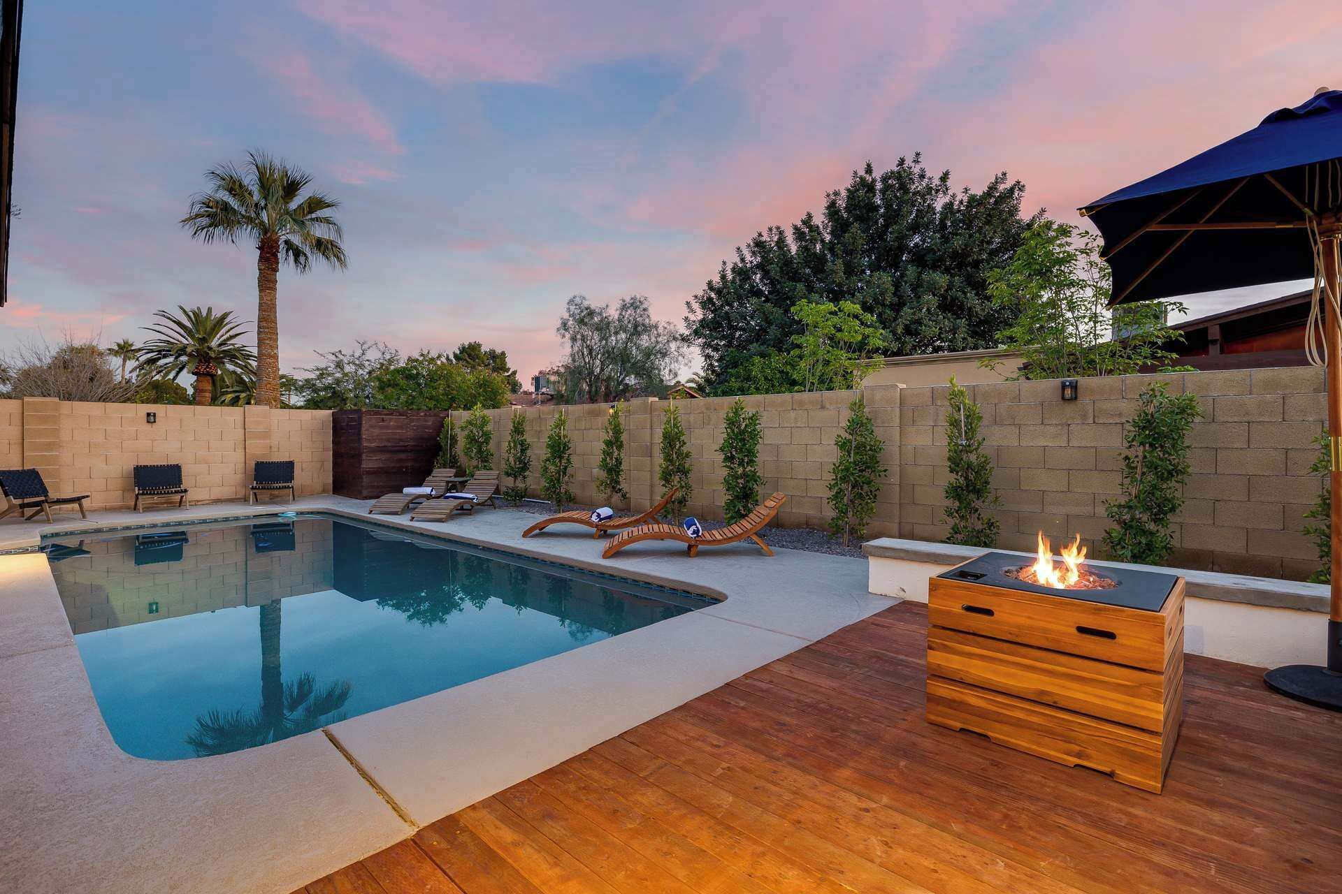 A swimming pool with lounge chairs and a fire pit.