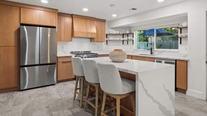 Une cuisine moderne avec des meubles en bois, un réfrigérateur en acier inoxydable, une cuisinière à gaz et un grand îlot central doté de tabourets de bar.