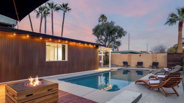 Un espace piscine extérieur moderne, doté d’une terrasse en bois, de chaises longues et d’un foyer.