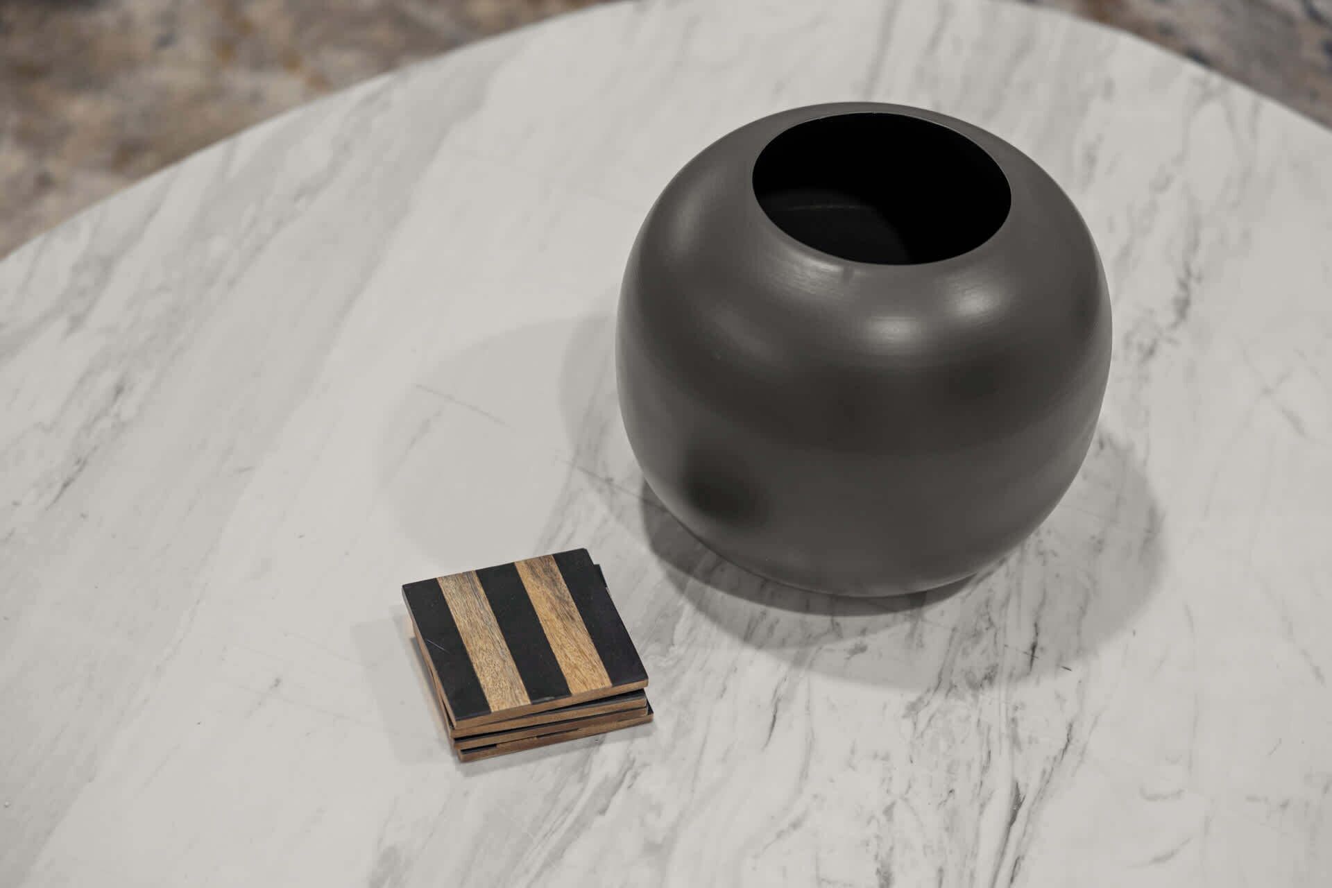 Una mesa de mármol con un jarrón gris oscuro y una pequeña caja de madera con detalles en listones negros y madera natural.