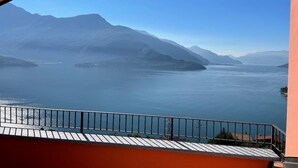 Blick von einem Balkon auf einen ruhigen See mit Bergen im Hintergrund.