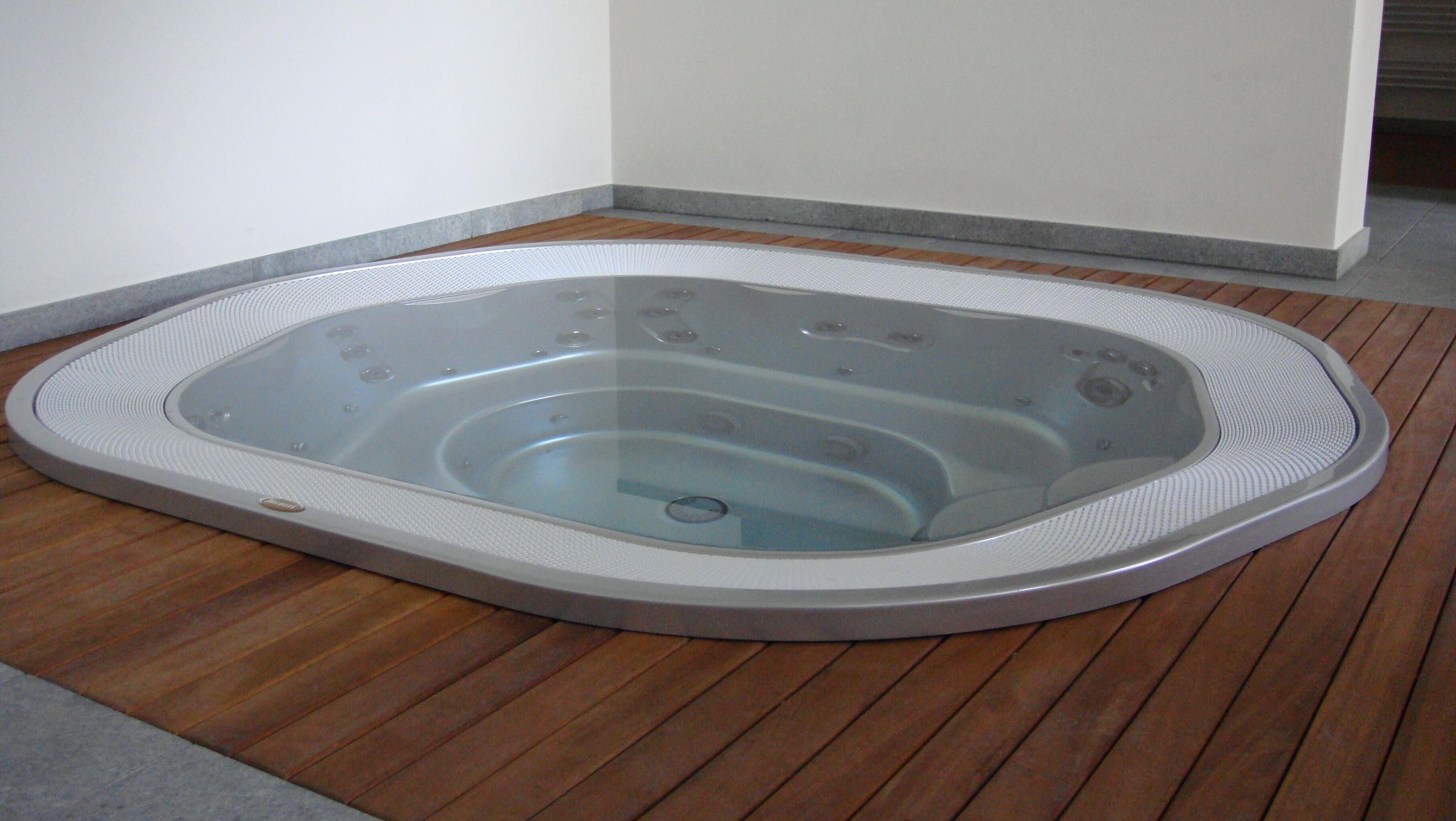 Un jacuzzi en una esquina con suelo de madera y pared blanca.