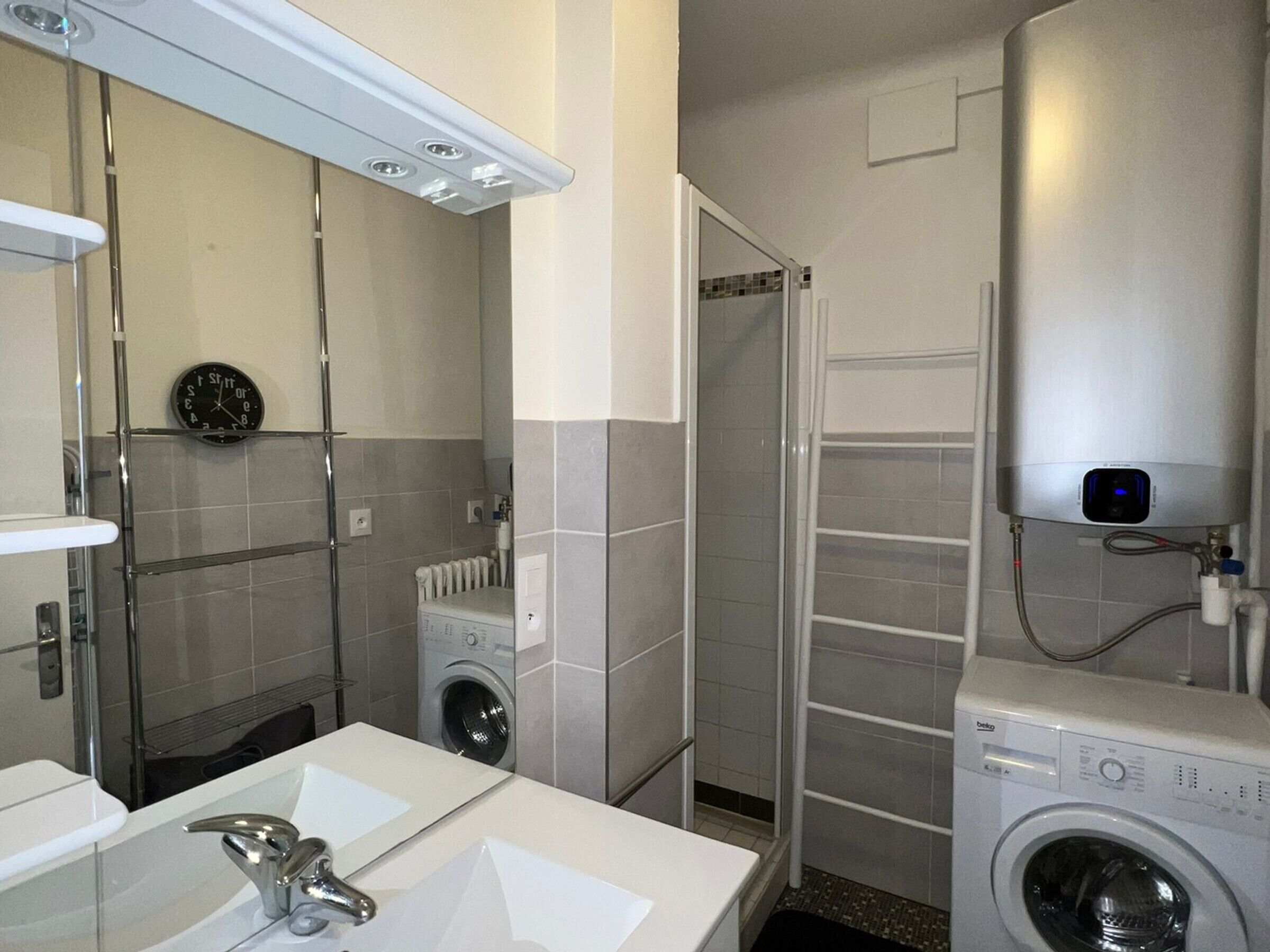 A modern bathroom with a sink, mirror, washing machine, and shower.