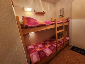 Ein Etagenbett mit einer rosa Decke, ein an der Wand befestigtes Regal und eine Leuchte.