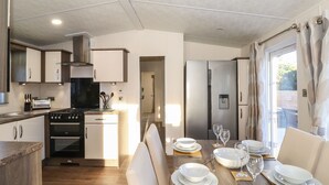 Una cocina moderna con estufa, horno y refrigerador, que da paso a un comedor con una mesa dispuesta para cuatro.