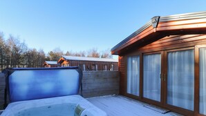 Un jacuzzi en una terraza de madera con vista a cabañas al fondo.