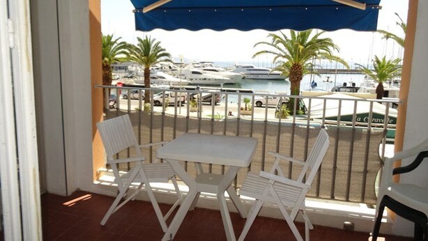 A balcony with a white table and chairs, overlooking a marina with boats and palm trees.