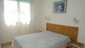 A bedroom with a bed, two bedside tables, a window with curtains, and a wall-mounted picture.