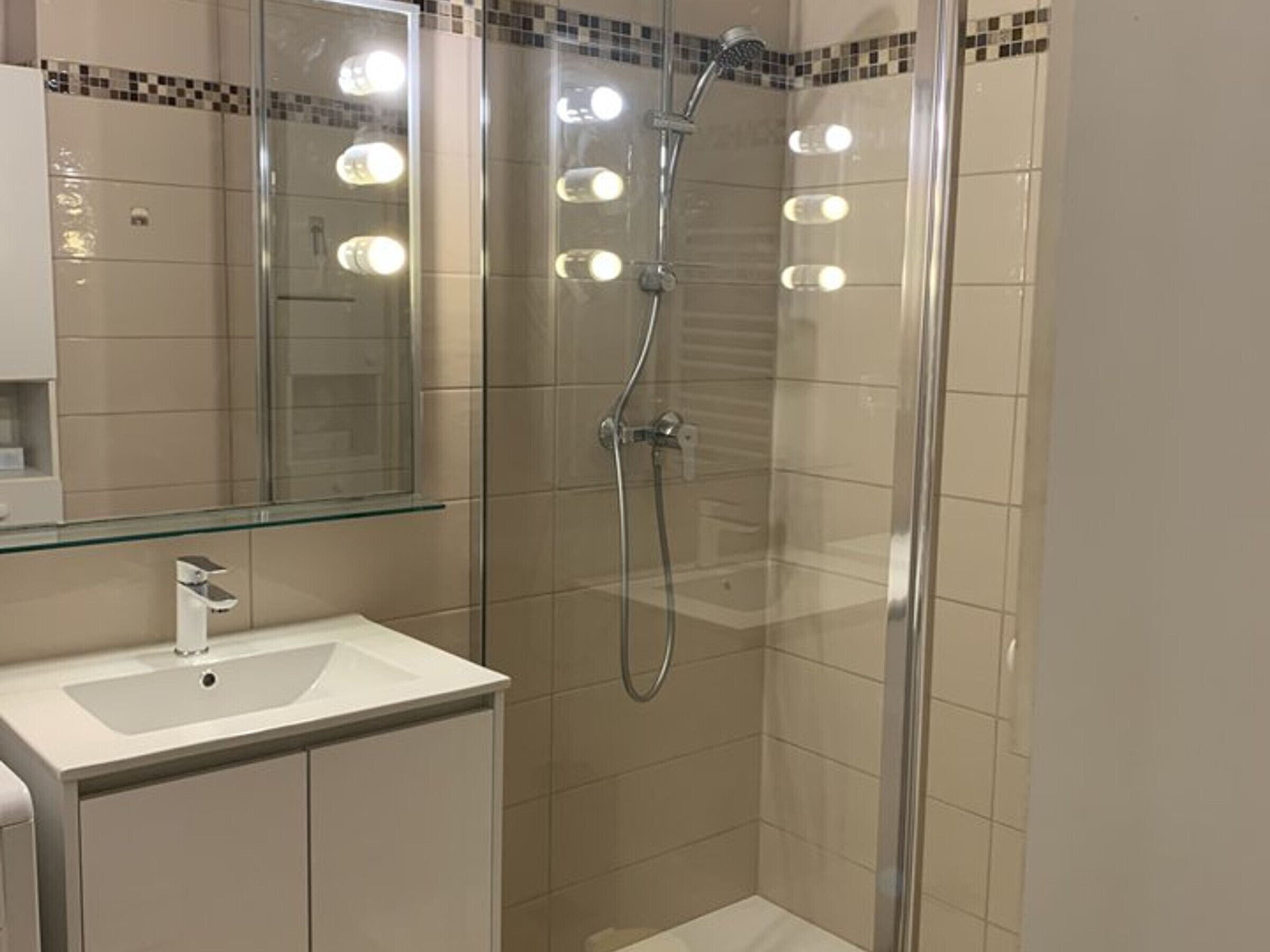Une salle de bain moderne avec une douche à parois de verre, un lavabo blanc et un miroir avec éclairage intégré.