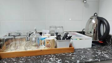 Un plan de travail de cuisine avec une machine à café, une bouilloire, ainsi que divers récipients et tasses.