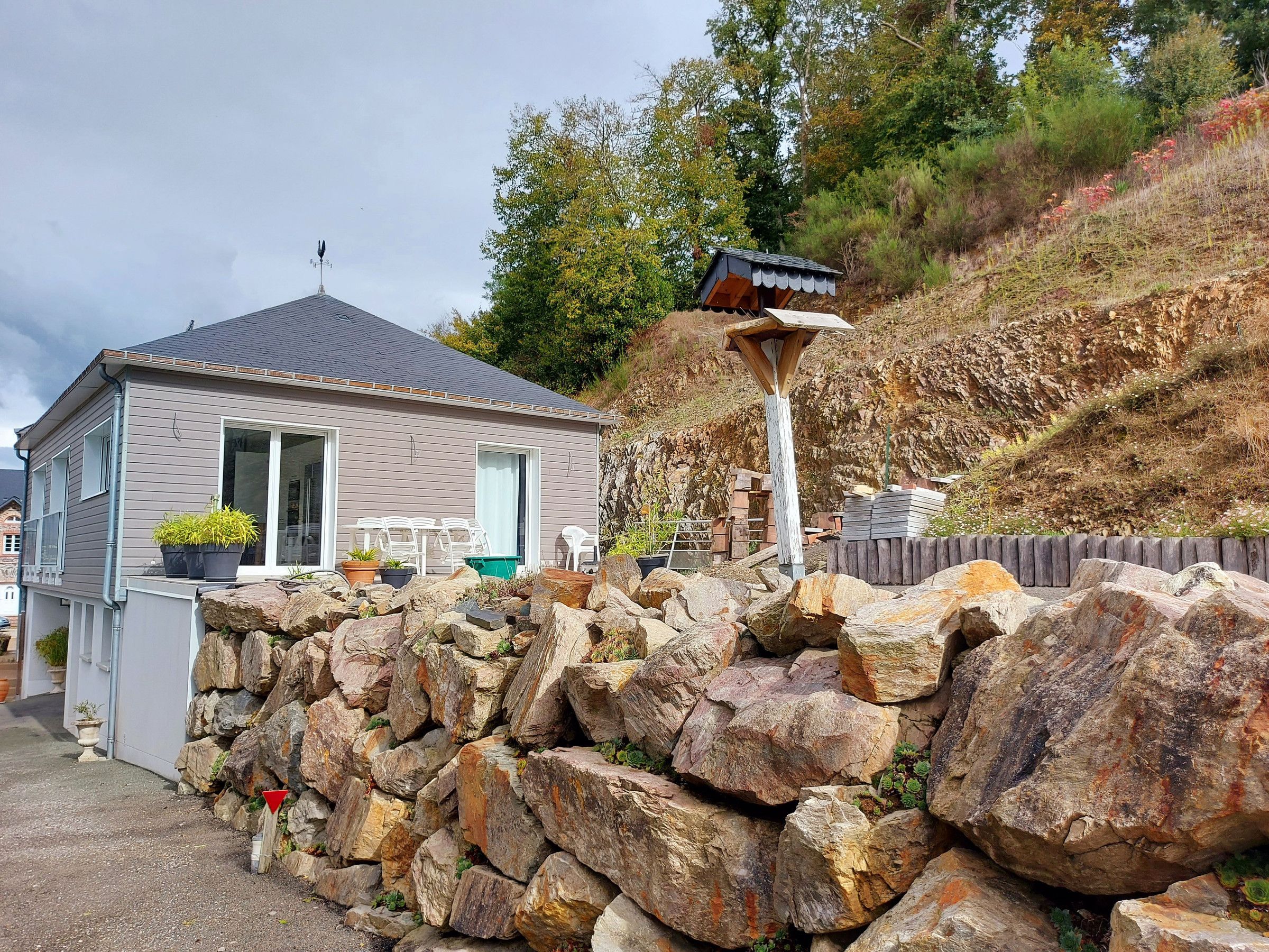 A house with a grey exterior, a tiled roof, and a stone wall in front.