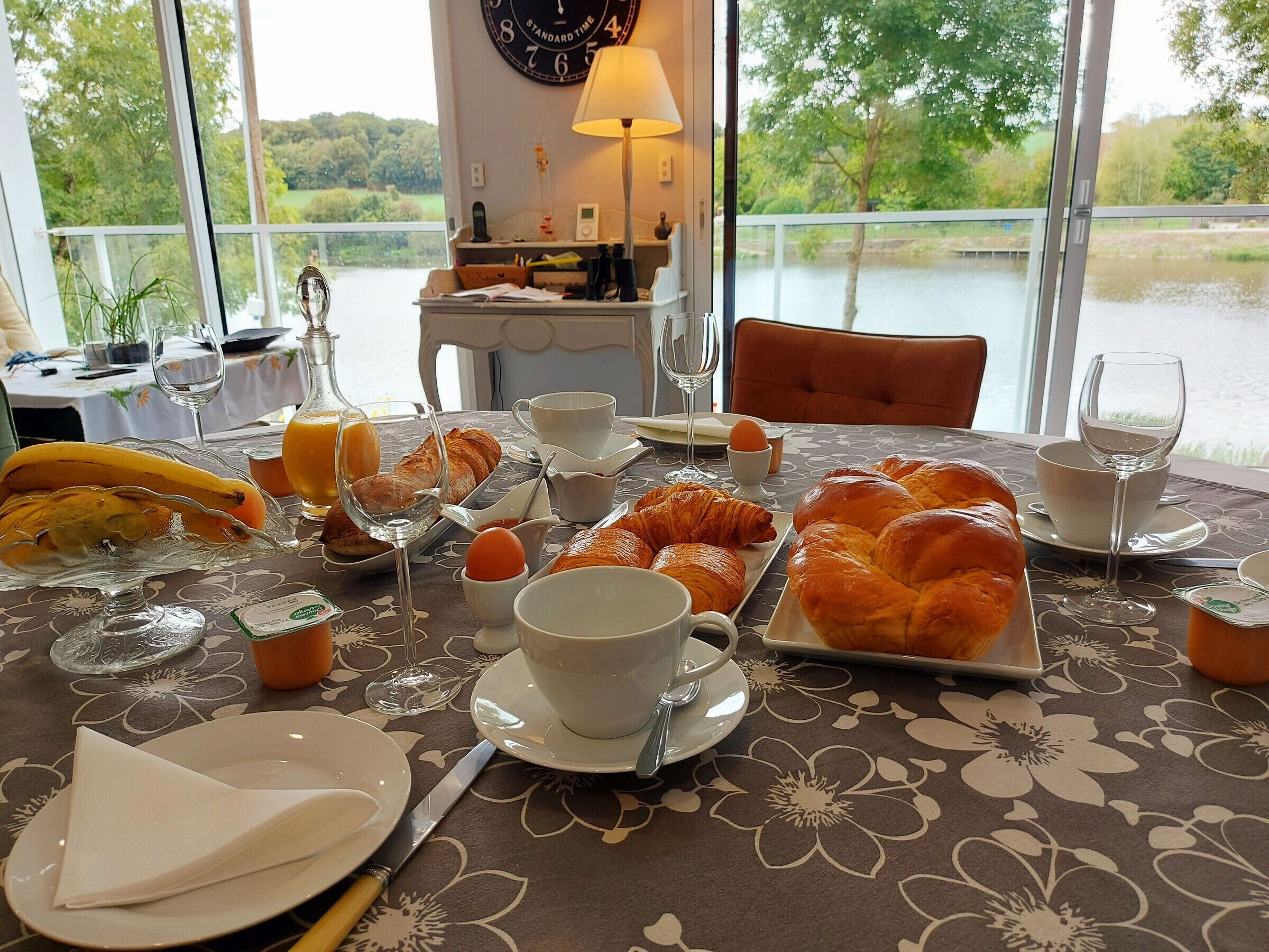 Een ontbijttafel met croissants, eieren en sapglazen, met uitzicht op een meer.
