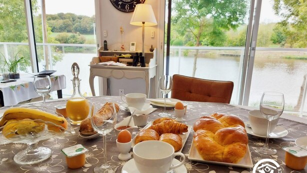 Een ontbijttafel met croissants, een banaan, sap en koffiekopjes, met uitzicht op een meer.