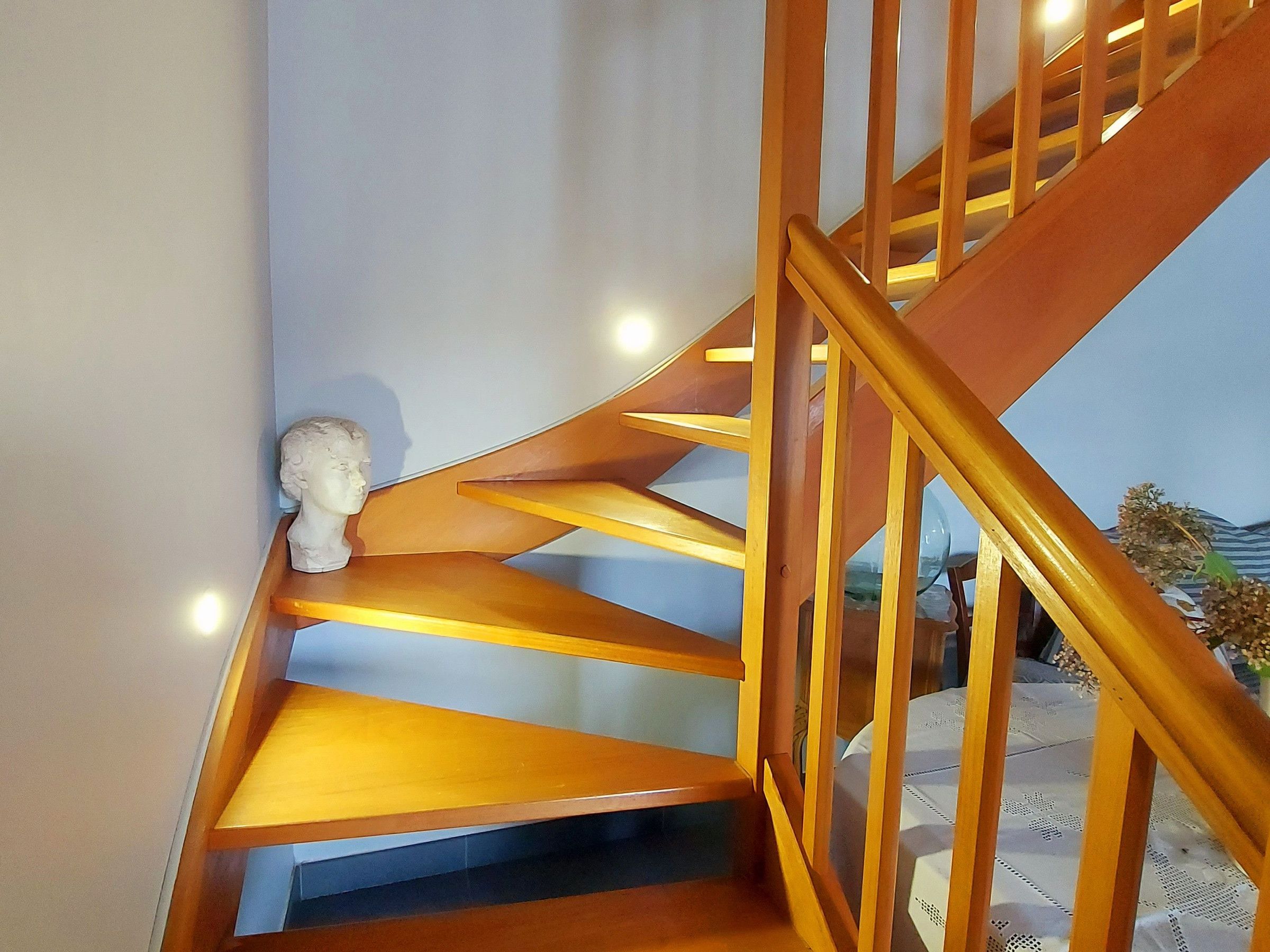 Un escalier en bois avec un buste sculpté, peint en blanc, accroché au mur.