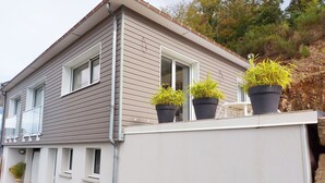 Een huis met twee verdiepingen, grijs beklede buitenmuren en witte sierlijsten. Er staan drie bloempotten op het balkon.