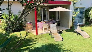 Eine Terrasse mit Esstisch, zwei Liegestühlen und einem Grill.