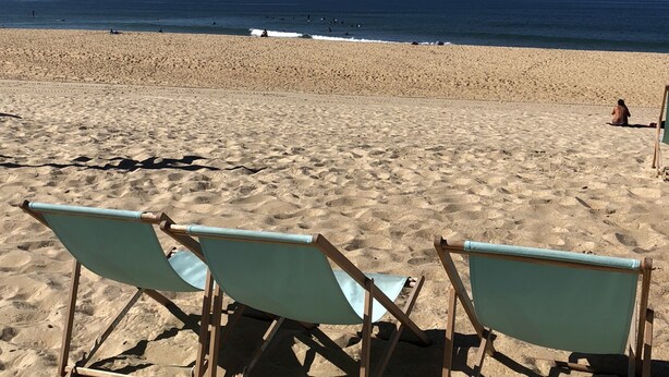 Ein Strand mit drei hellblauen Liegestühlen und Sand.