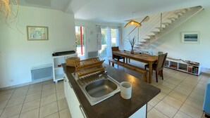 Eine moderne Küche mit einer zentralen Kochinsel, einem Essbereich mit Holztisch und einer Treppe zu einer oberen Ebene.