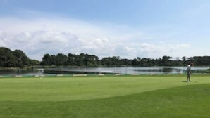 Ein Golfplatz mit einem Wasserspiegel im Hintergrund und einer Person auf dem Grün.