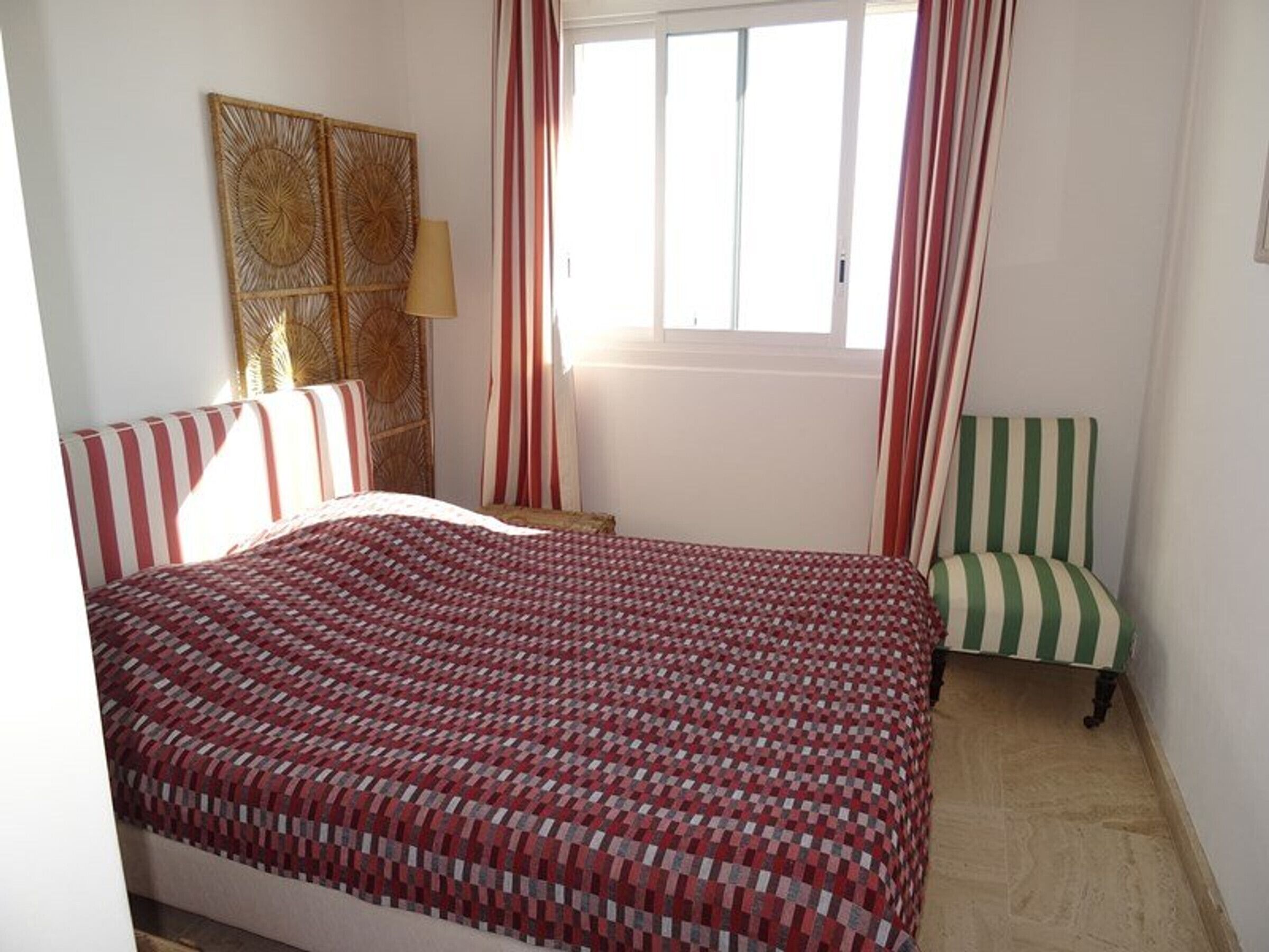 A bedroom with a bed, a chair, a window with curtains, and a wall decoration.
