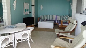 A living room with a teal wall, white furniture, a round table, and a sofa with striped cushions. - Hyères Port T2 with Air Conditioning and Wifi, Sea View (Hyères)