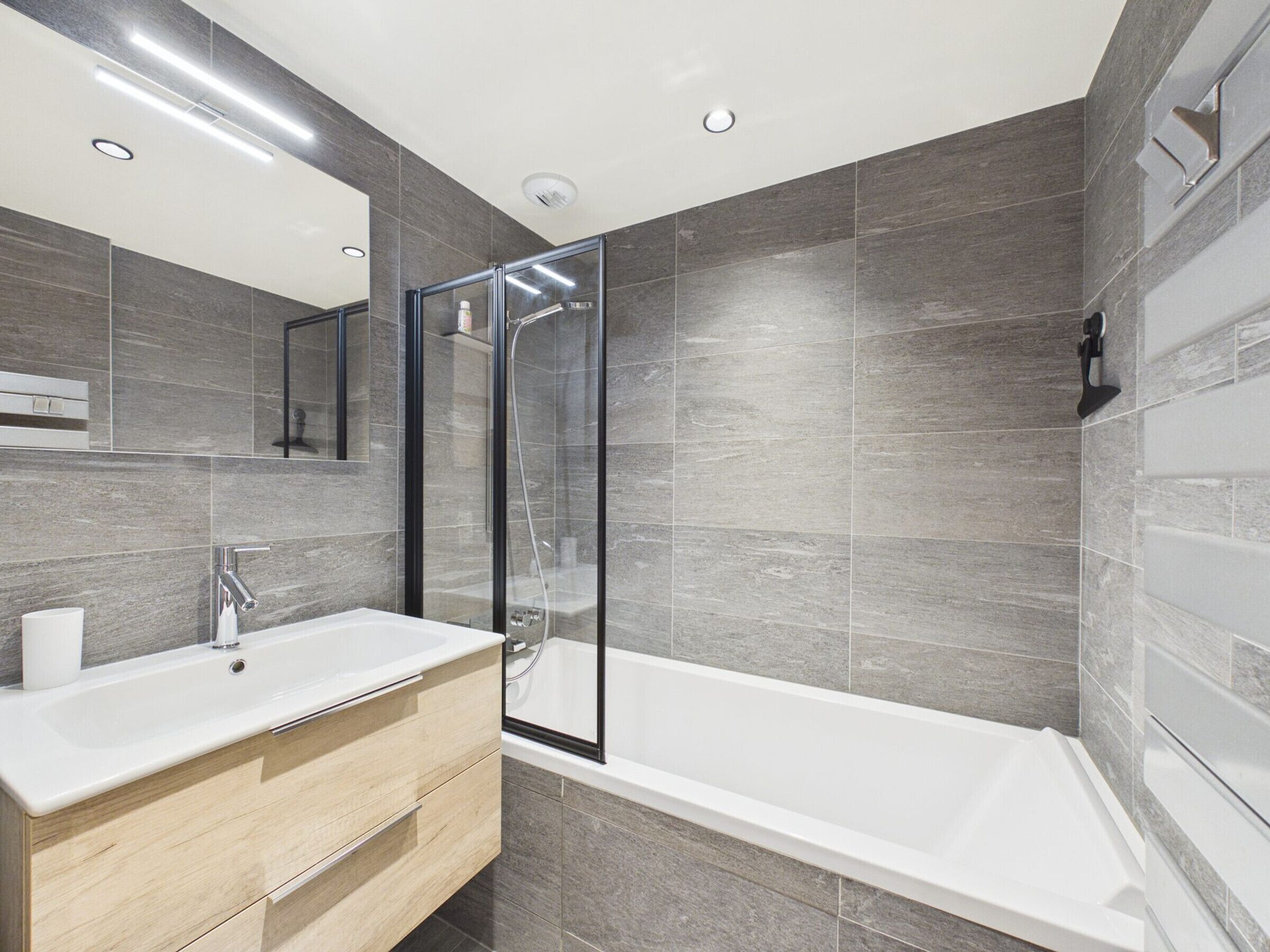Une salle de bain moderne avec une douche à l’italienne en verre, une baignoire blanche et un meuble-lavabo en bois.