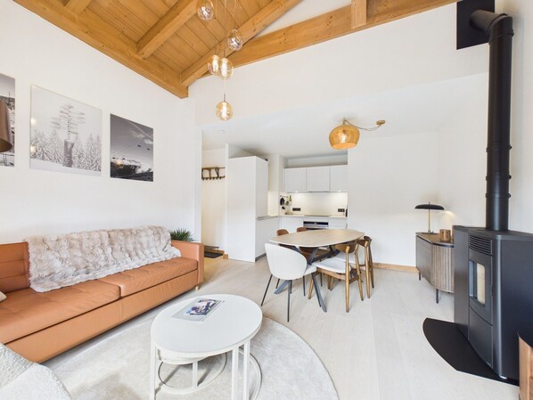 A modern living room with a sofa, a round table, and a kitchen area with a stove.