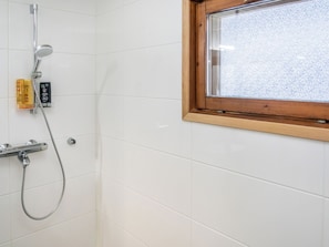 Chuveiro com chuveiro manual e painel de controle fixado na parede, janela com moldura de madeira e paredes revestidas de azulejo branco.