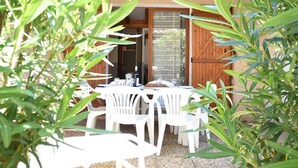 An outdoor patio with a table and chairs, a wooden door, and a view of the surrounding greenery. - Cozy Studio House with Mezzanine & Cabine - 6 Beds, 40m from Water, 3min to Beach, Parking Included (Gruissan)