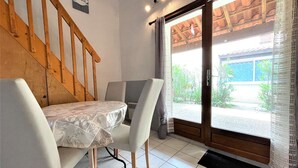 A dining area with a table and chairs, a wooden staircase, and a sliding glass door leading to an outdoor area. - Cozy Studio House with Mezzanine & Cabine - 6 Beds, 40m from Water, 3min to Beach, Parking Included (Gruissan)