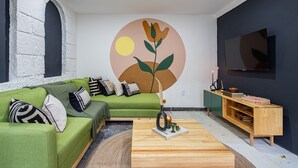 A living room with a green sofa, a wooden coffee table, a TV, and a wall with a circular design. - Sleeps 9 Outdoor Space PingPong Table (Oaxaca)
