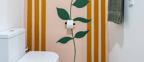 Un baño con inodoro, una toalla colgada en la pared y una pared decorativa con rayas y diseño de hojas.