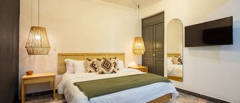 A bedroom with a bed, bedside lamps, a ceiling fan, a TV, and a door.