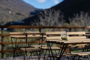 Ein Holztisch mit einem Glas, das eine Pflanze enthält, draußen aufgestellt mit Bänken und einem Bergpanorama.
