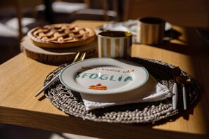 A table with a plate labeled "SFOGLIA," a pie, a striped mug, and cutlery. - Tenuta Pascarella Bed And Breakfast (Frasso Telesino)