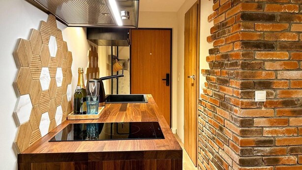 A modern kitchen with a wooden countertop, a built-in stove, and a brick wall. - Beautiful 1-bed Apartment in Klaipeda (Klaipeda)