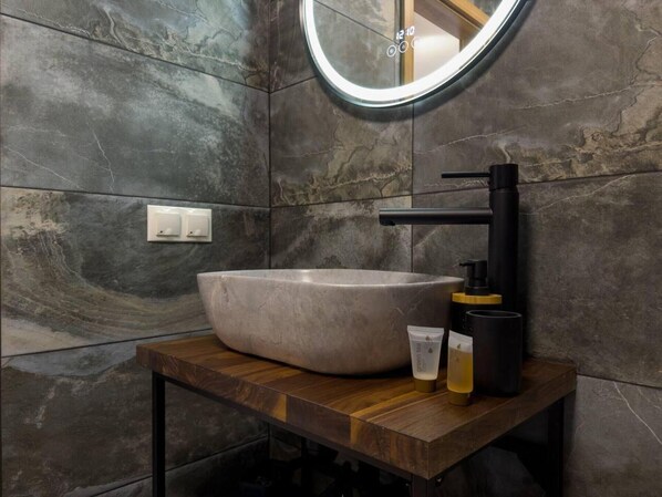 A modern bathroom with a large, oval-shaped sink, a round mirror, and a wooden vanity. - Beautiful 1-bed Apartment in Klaipeda (Klaipeda)