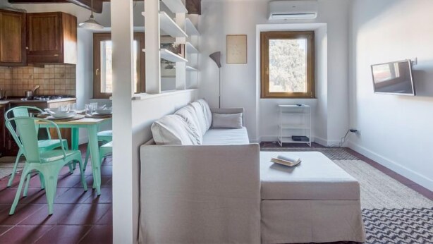 Ein kompakter Wohnbereich mit Küchenzeile, Essbereich mit Tisch und Stühlen, einer Couch, einem an der Wand befestigten Fernseher und einem Fenster für natürliches Licht.
