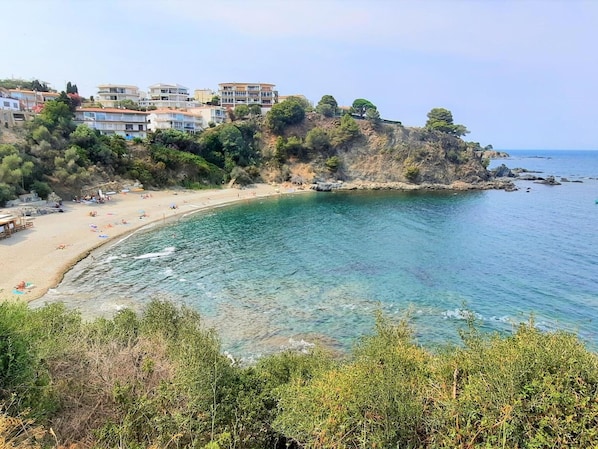 A coastal view with a beach, clear water, and buildings on a hillside.