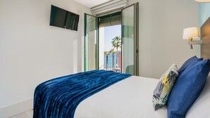 Habitación de hotel con cama, televisión montada en la pared y vistas a palmeras a través de una puerta abierta.
