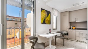 Un apartamento moderno con balcón, zona de comedor con mesa y sillas, cocina con armarios y un amplio ventanal con persianas.