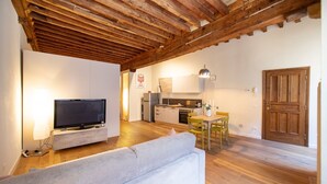 A modern living room with a sofa, a flat-screen TV, wooden flooring, and a kitchen in the background. - Dante´s Home Cozy in Center Town (Lucca)